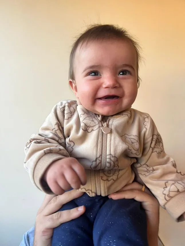 Joy sorrindo largo, no colo, de pijama de leõezinhos.