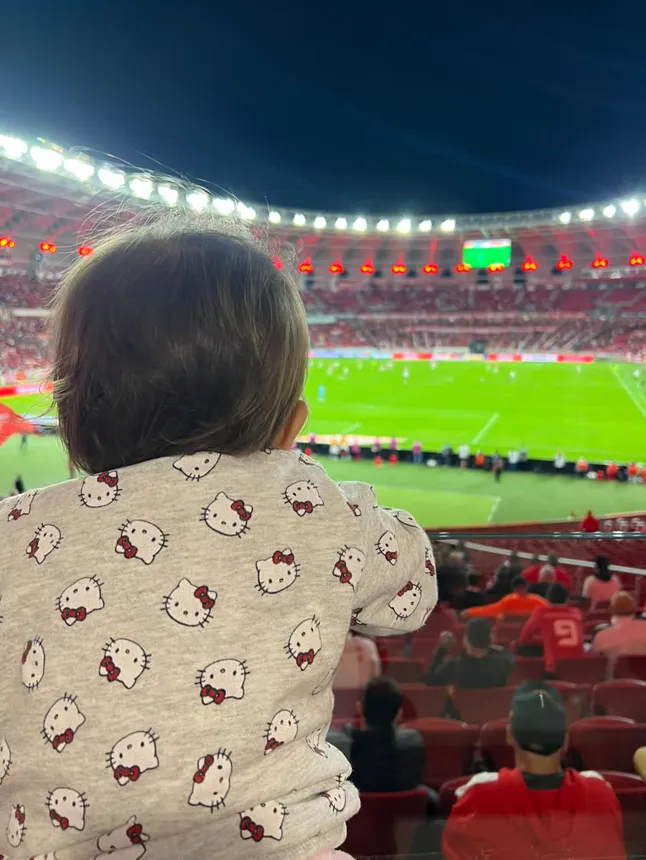 Joy de costas, olhando o gramado iluminado do estádio.